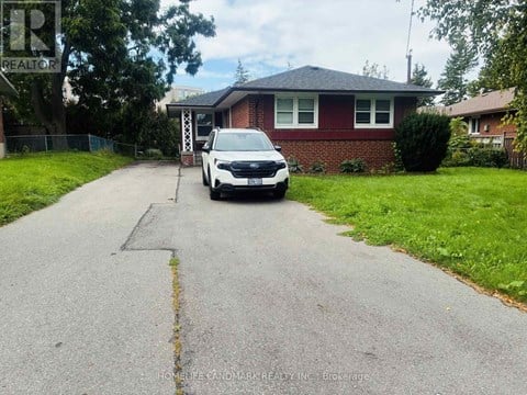 A white car is parked in front of a red brick house.