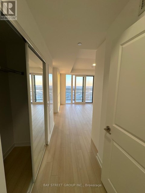 A hallway with wooden floors and white walls leading to a door.