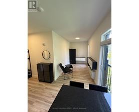 A black chair is in a white room with wood flooring.