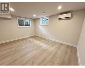 A spacious room with wooden flooring and two windows.
