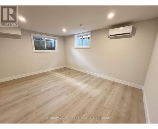 A spacious room with wooden flooring and two windows.