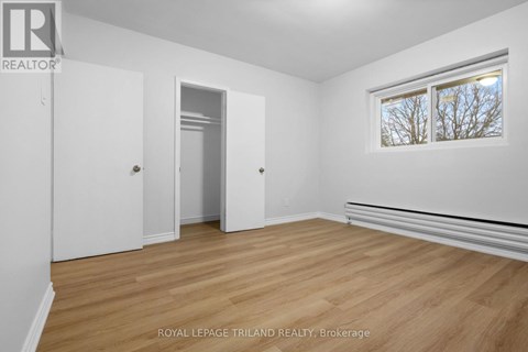A white room with wooden floors and a window showing bare trees outside.