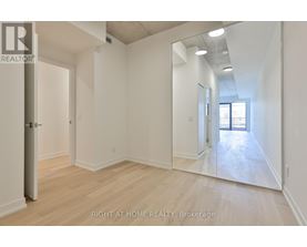 A spacious room with wooden flooring and white walls, with a door on the left and a mirror on the right.