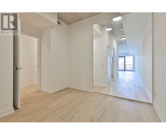 A spacious room with wooden flooring and white walls, with a door on the left and a mirror on the right.