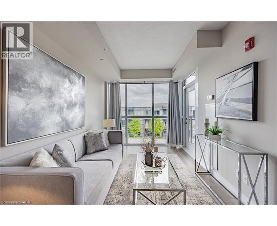 A well-lit, modern living room with a grey sofa, a glass coffee table, and a large painting on the wall.