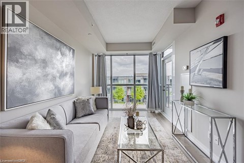 A well-lit, modern living room with a grey sofa, a glass coffee table, and a large painting on the wall.