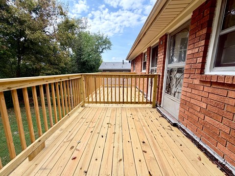 A wooden deck is in front of a red brick house.