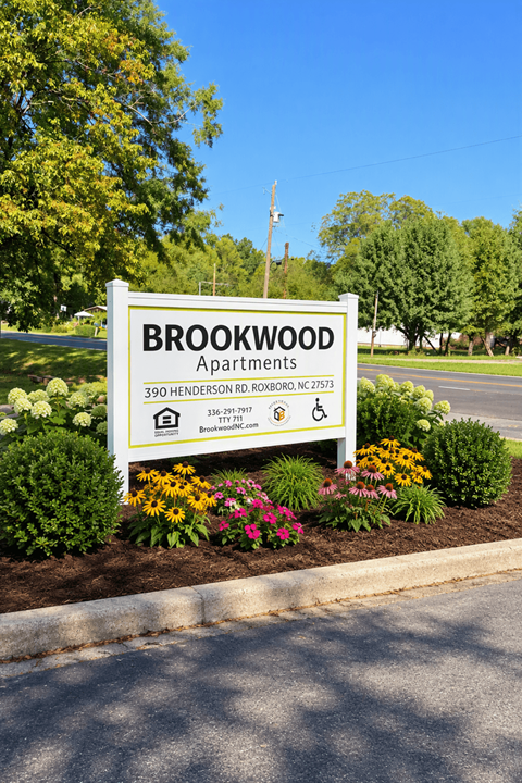 A sign for Brookwood Apartments is surrounded by flowers and greenery.