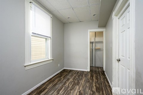 A room with wooden floors and white walls, with a window on the left and a door on the right.