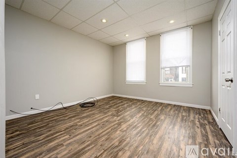 A room with wooden flooring and two windows.