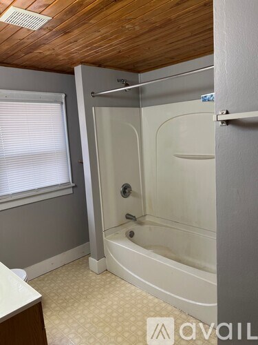 A bathroom with a white tub and a window with blinds.
