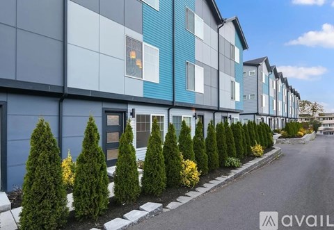 A row of modern townhouses with a sidewalk and landscaping.