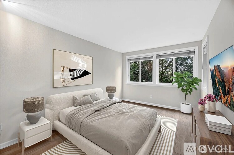 A bedroom with a large bed, a nightstand with a lamp, a side table with a plant, and a painting on the wall.