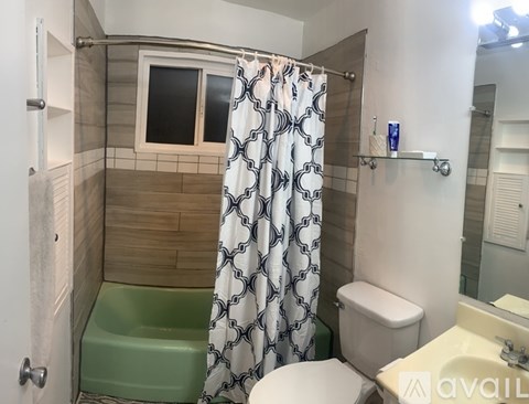 A bathroom with a green tub, a white toilet, and a shower with a patterned curtain.