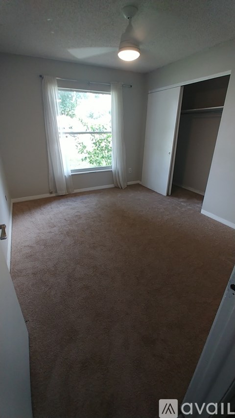 A room with a carpeted floor and a window with white curtains.