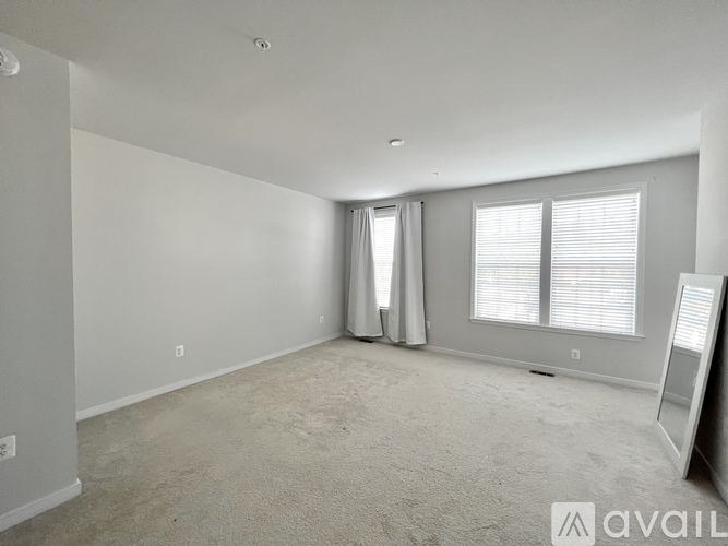 A spacious room with a carpeted floor and a window with white blinds.