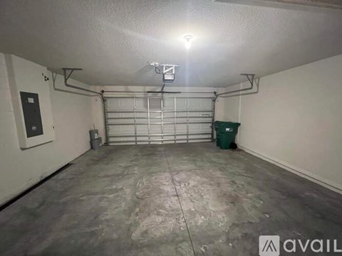 A spacious garage with a closed white door and a green trash can.