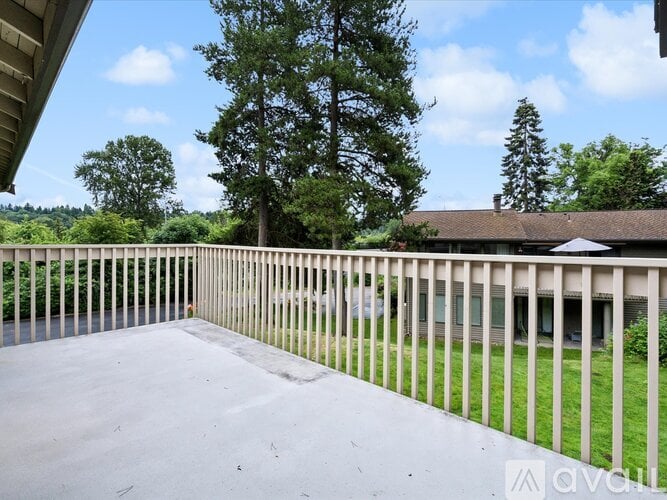 A balcony with a white railing overlooks a green lawn and trees.