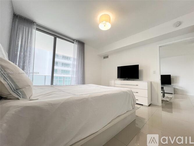 A bedroom with a large bed, a flat-screen TV, and a window with curtains.