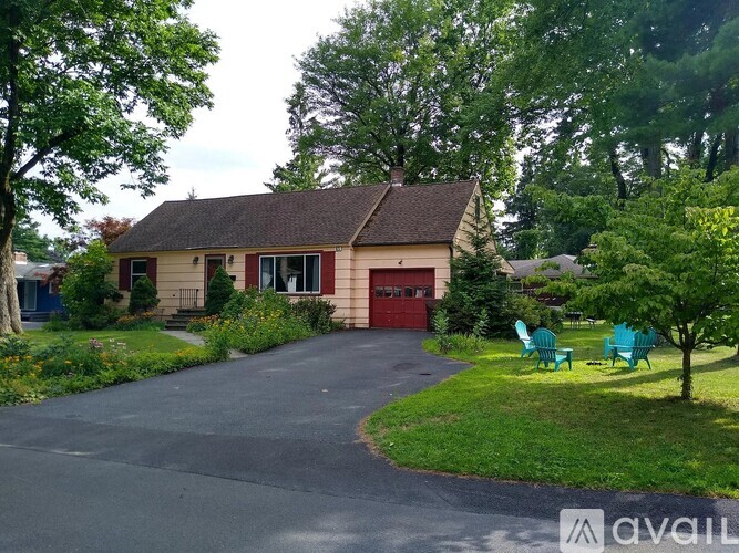 A house with a red door is surrounded by greenery and has a driveway leading to it.