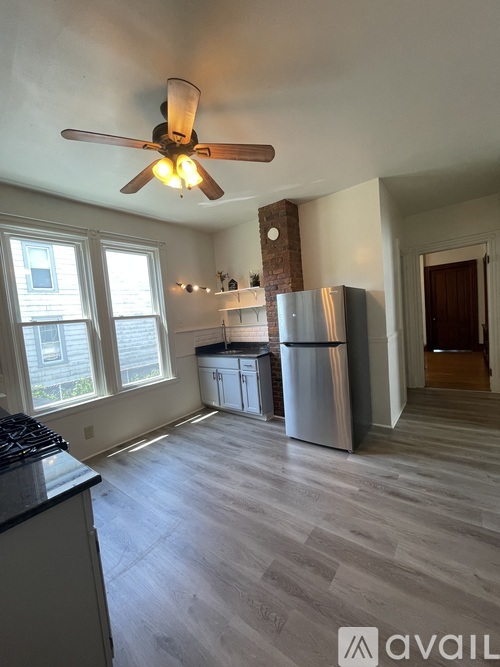 A kitchen with a fan on the ceiling and a refrigerator in the corner.