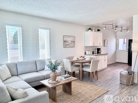 A living room with a grey sofa, a wooden coffee table, and a dining table set up in the background.