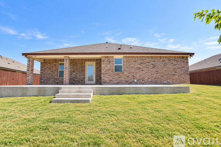 A house with a brown brick exterior and a white door is surrounded by a grassy lawn.