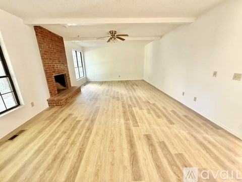 A spacious room with wooden flooring and a brick fireplace.