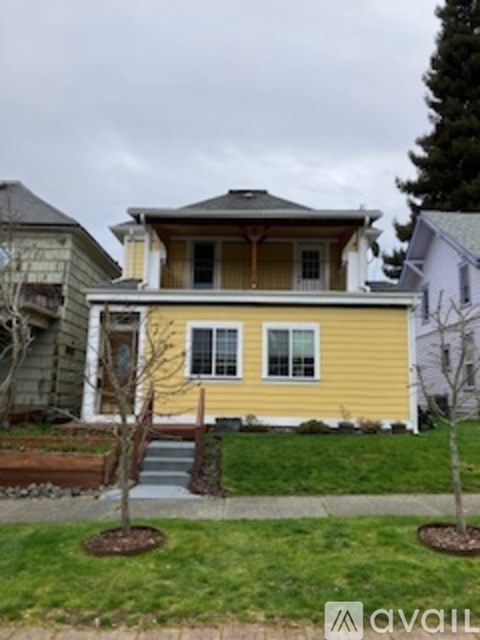 A yellow house with a porch and a tree in front.