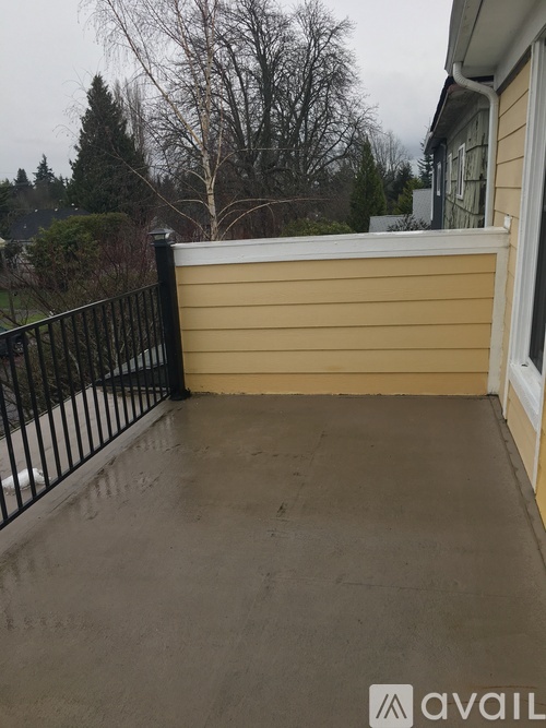 A patio with a black railing and a view of trees and a house.