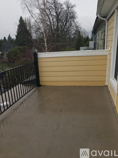 A patio with a black railing and a view of trees and a house.
