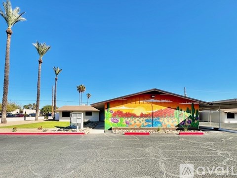 A building with a colorful mural on the side is surrounded by palm trees.