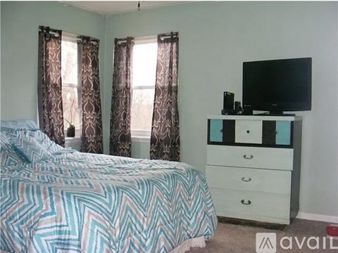A bedroom with a bed, dresser, and window with curtains.
