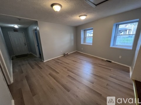 A room with wooden flooring and two windows.