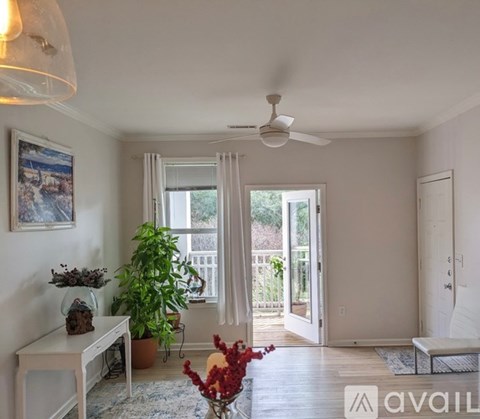 A living room with a ceiling fan, a painting on the wall, a potted plant, and a vase with flowers on the table.