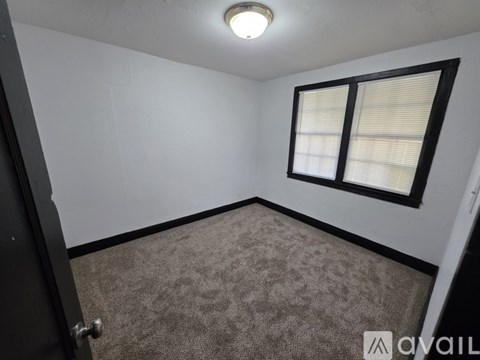 A room with a carpeted floor, a window with blinds, and a door.