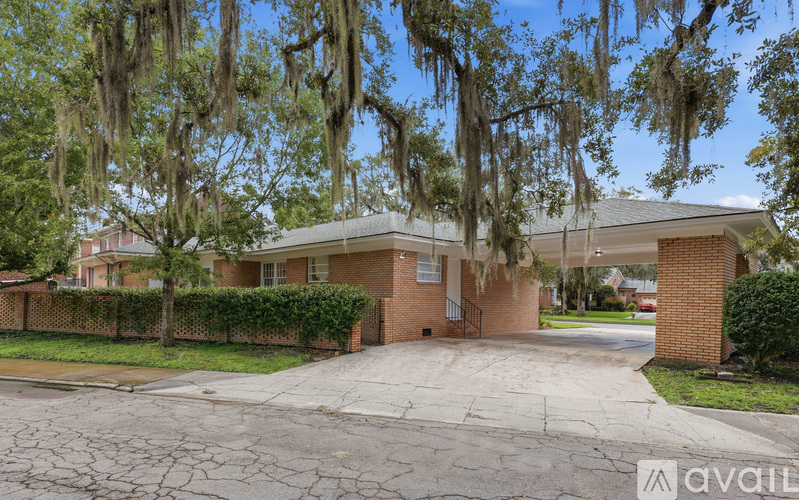 A house with a driveway and trees with Spanish moss hanging from them.