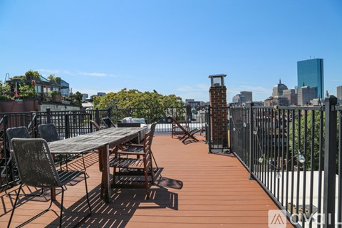 A wooden table and chairs are set up on a deck with a city skyline in the background.