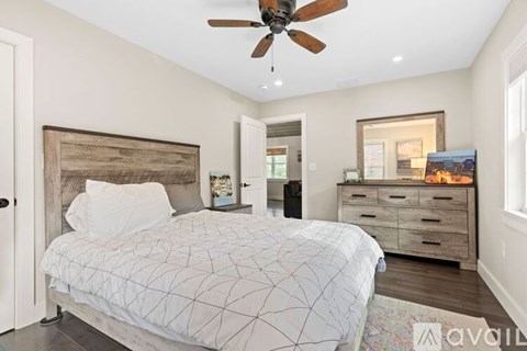 A bedroom with a large bed, a ceiling fan, and a dresser with a mirror above it.