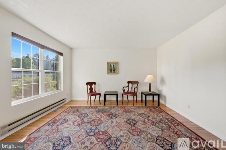 A living room with a rug, two chairs, and a table with a lamp.