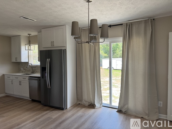 A kitchen with a refrigerator, cabinets, and a window with curtains.
