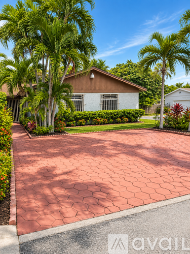 A house with a red brick driveway and palm trees in the background.