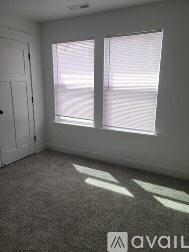 A room with a carpeted floor, a door, and a window with blinds.