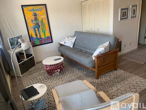 A living room with a grey couch, a painting on the wall, and a patterned rug.