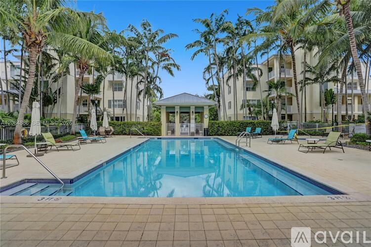 A pool surrounded by palm trees and lounge chairs with a building in the background.
