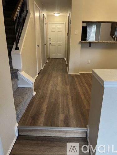 A hallway with wood flooring and a staircase with a metal railing.