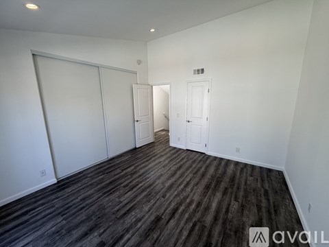 A room with wooden flooring and white walls, with two doors and one window.
