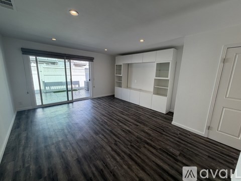 A spacious room with wooden flooring and white walls.