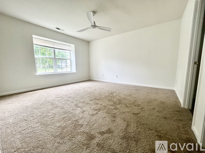 A room with a carpeted floor, a ceiling fan, and a window.