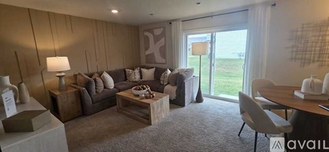 A living room with a grey couch, a wooden coffee table, and a large window with a view of the lawn outside.